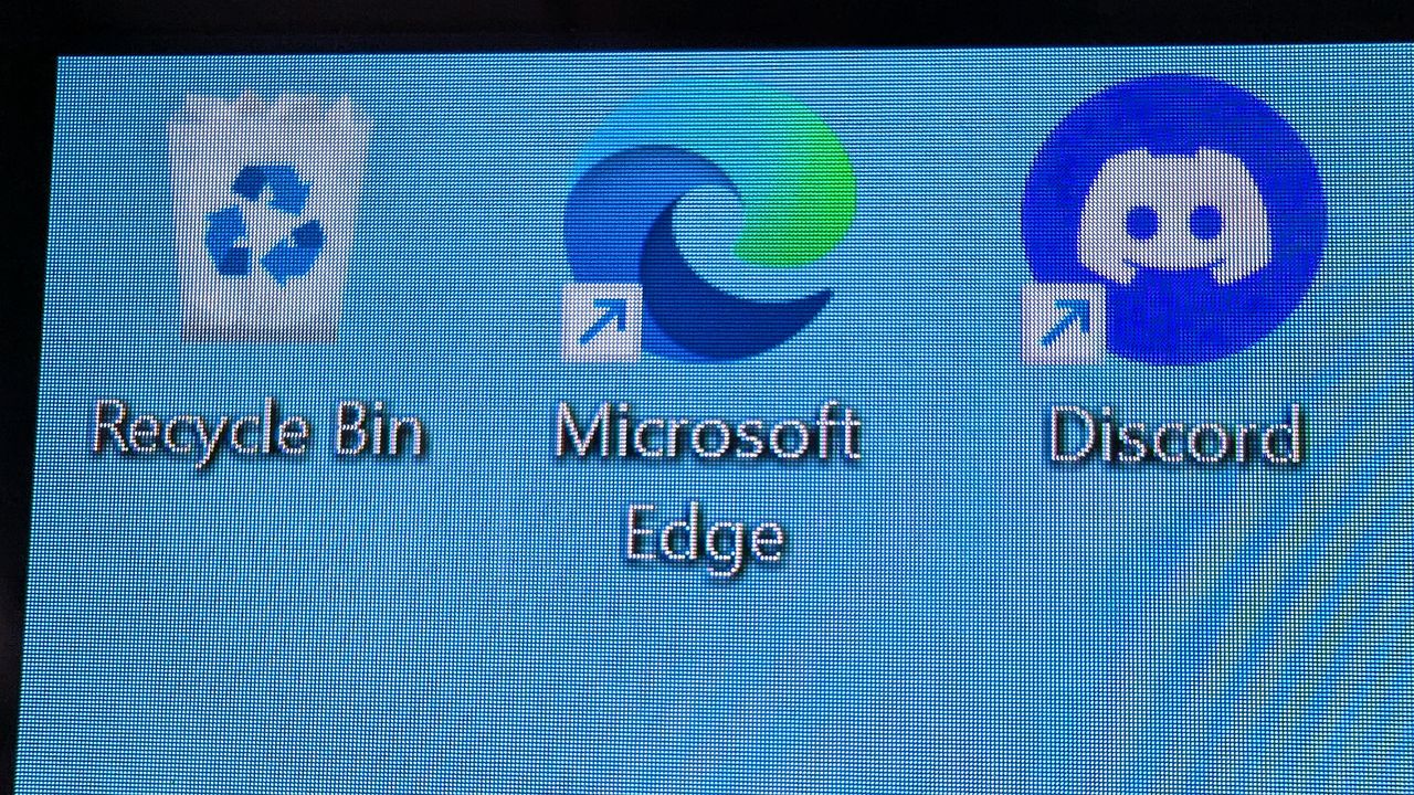 A close‑up of the ASUS ROG Strix OLED XG32UQWMS monitor showing a Windows desktop with Recycle Bin, Microsoft Edge, and Discord icons against a light blue background.