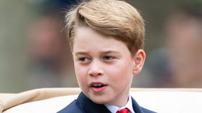 Prince George wearing a suit and red tie looking to the side