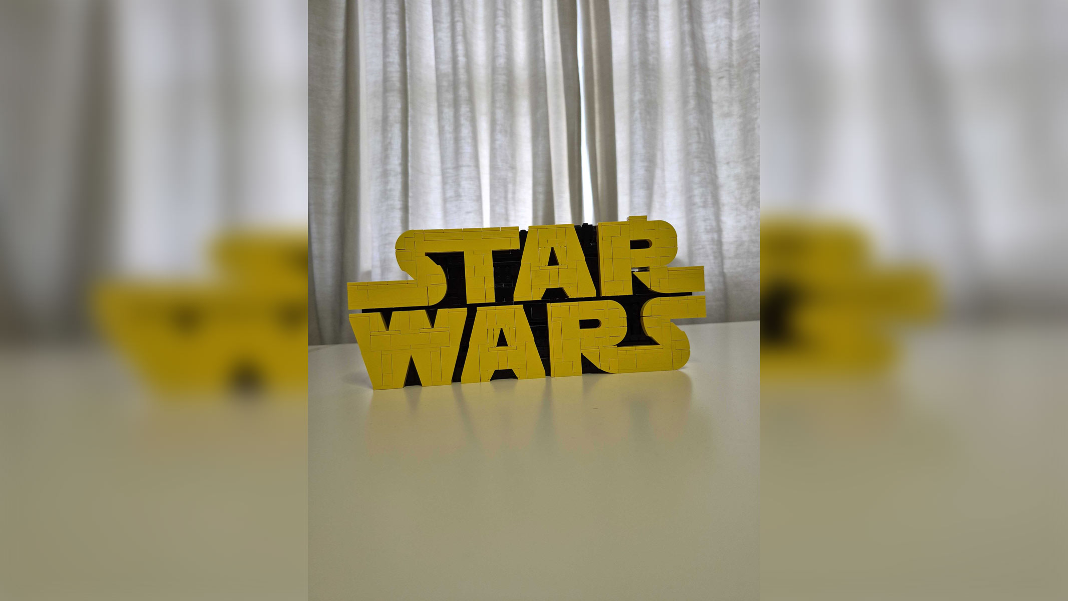 The Lego Star Wars Logo set in its completed form on a white table with white curtains behind it.