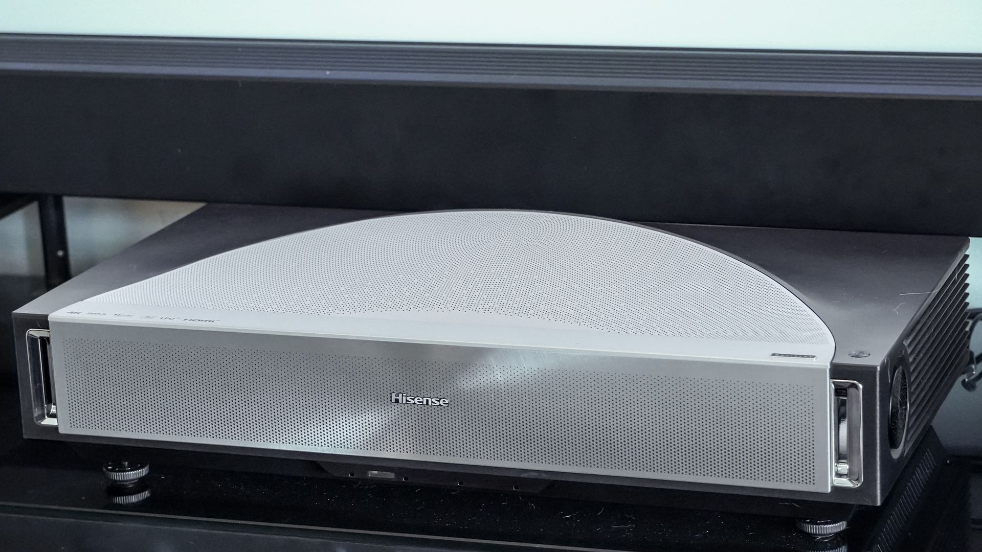 A Hisense PX4 Pro projector on a home media center shelf