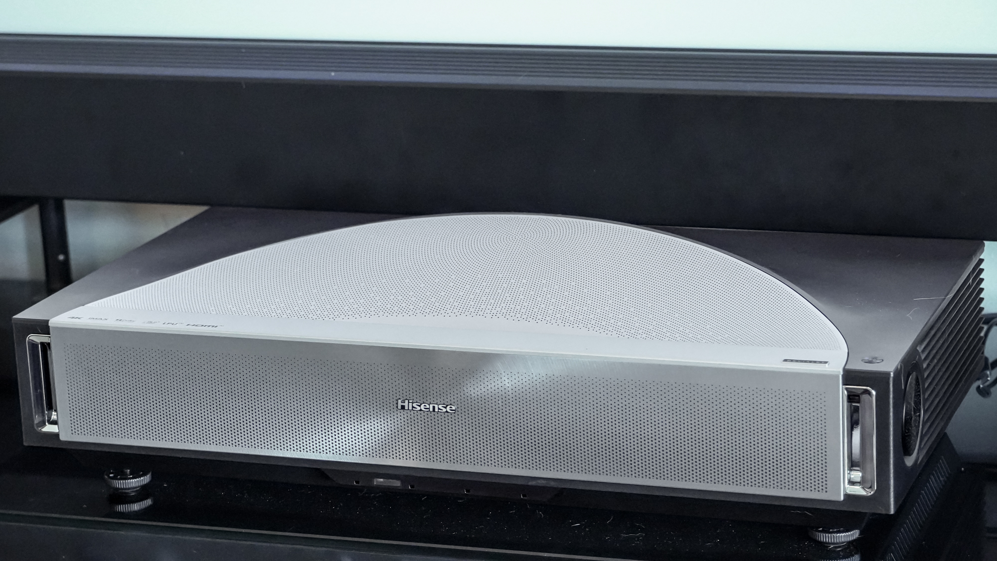 A Hisense PX4 Pro projector on a home media center shelf