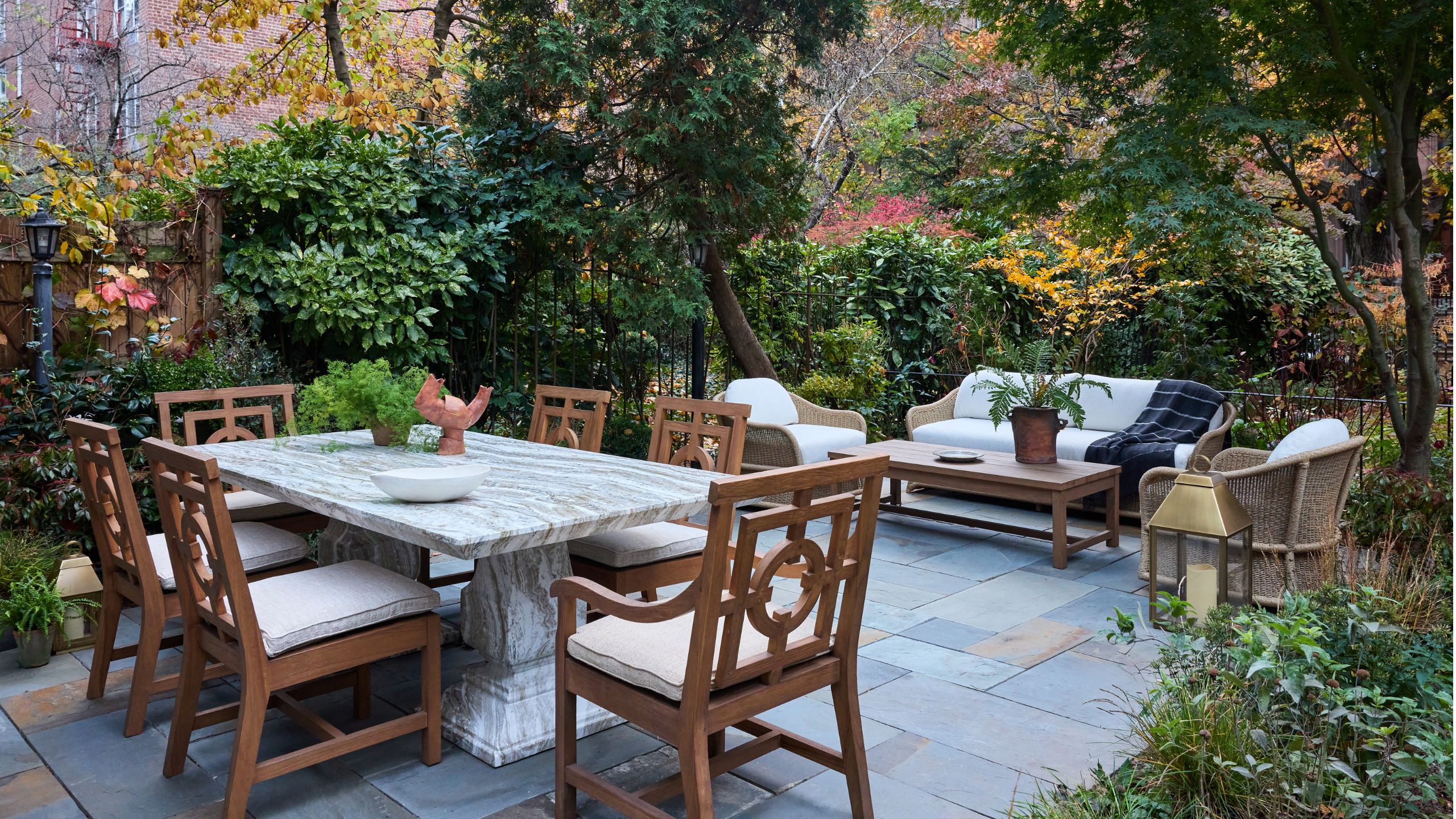 an enclosed garden in Brooklyn with paved patio and wooden furniture with a large marble table