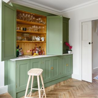 green kitchen cupboards opening to reveal hidden bar with drinks and glasses