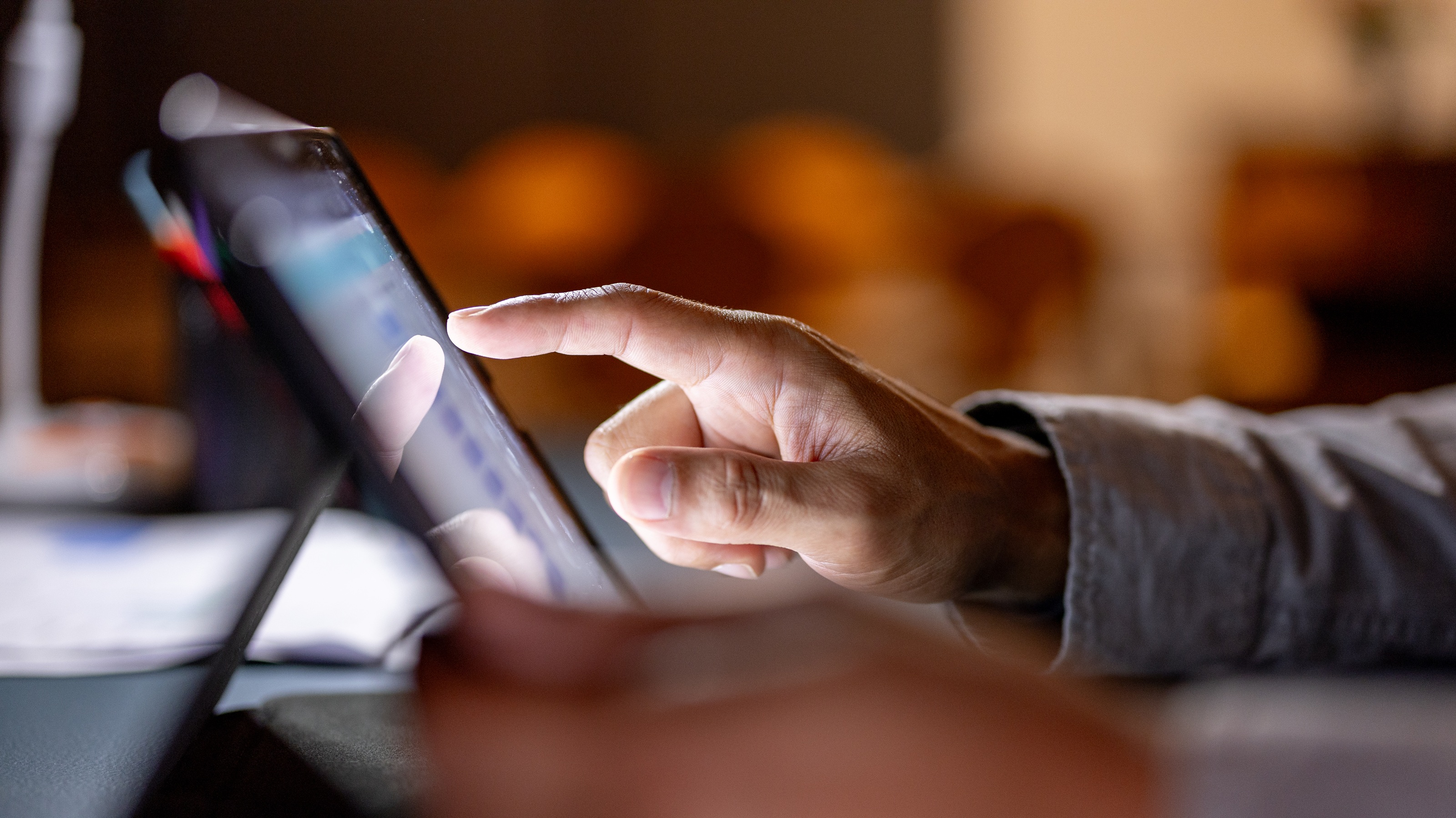 A man does research on a tablet at his desk, only his hand and forearm showing.