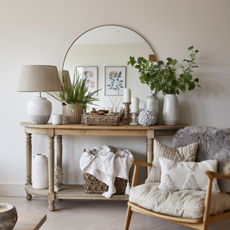 Circular mirror in neutral room. There is side table with decoration in front of of it and a comfy neutral rocking chair to the side.