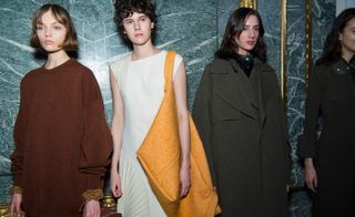 Models are seen wearing thick-knit sweaters and outerwear, matched with a large vibrant duvet bag