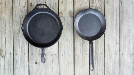 Cast iron pan beside carbon steel pan on wooden table