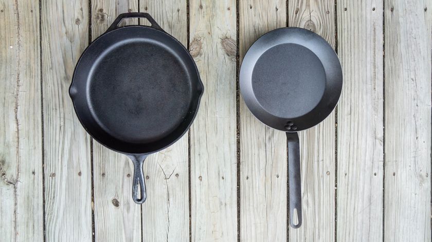 Cast iron pan beside carbon steel pan on wooden table