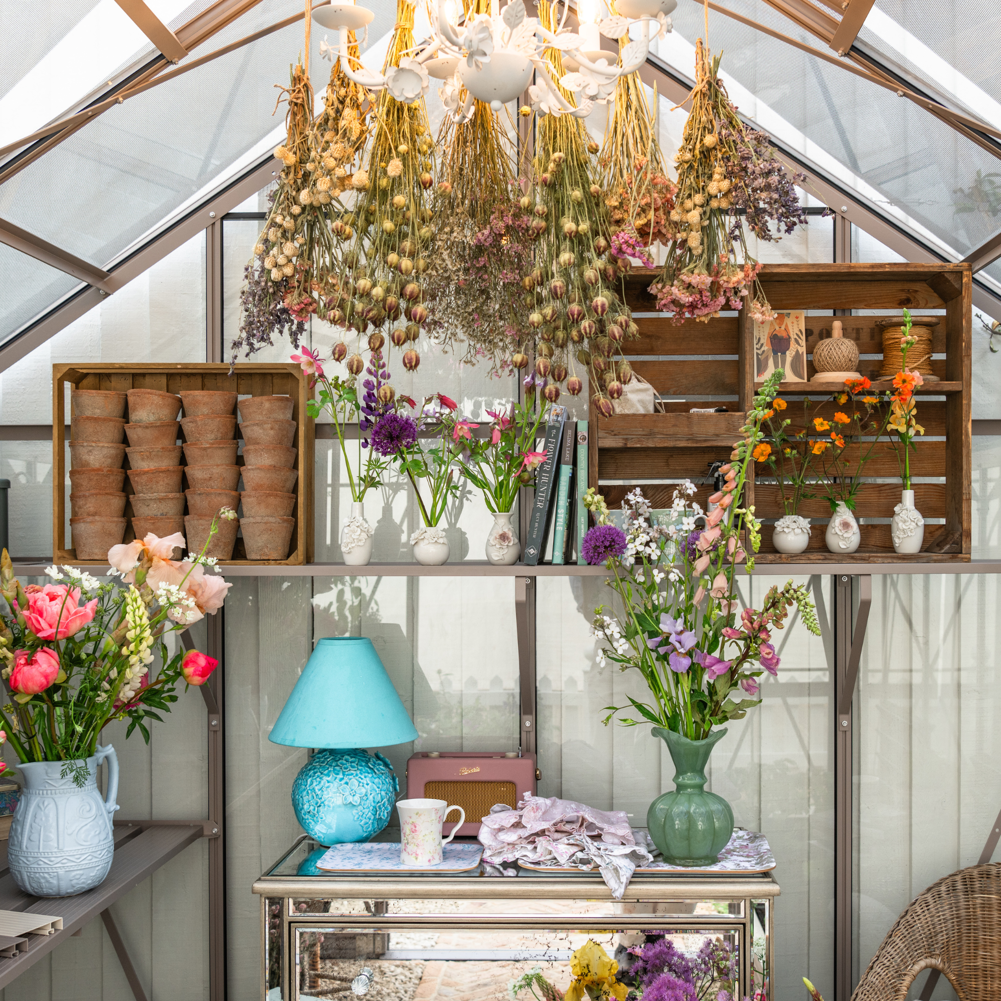 Inside a greenhouse decorated wit vases, a turquoise lamp and flowers.