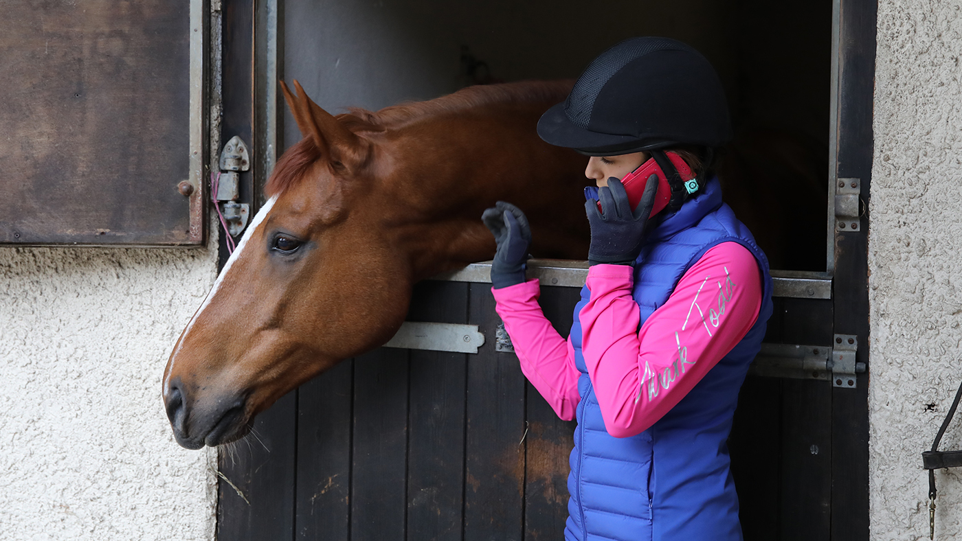 Rider on phone outside horse&rsquo;s stable