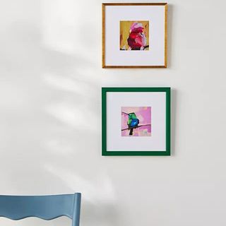 Two small colorful framed paintings above a light blue dining chair