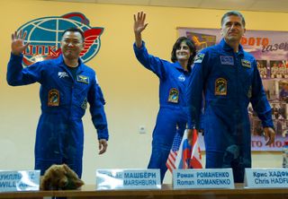 Quarantined Expedition 32 prime crew members wave goodbye from behind glass during a prelaunch press conference held at the Cosmonaut Hotel on Friday, July 13, 2012 in Baikonur, Kazakhstan.