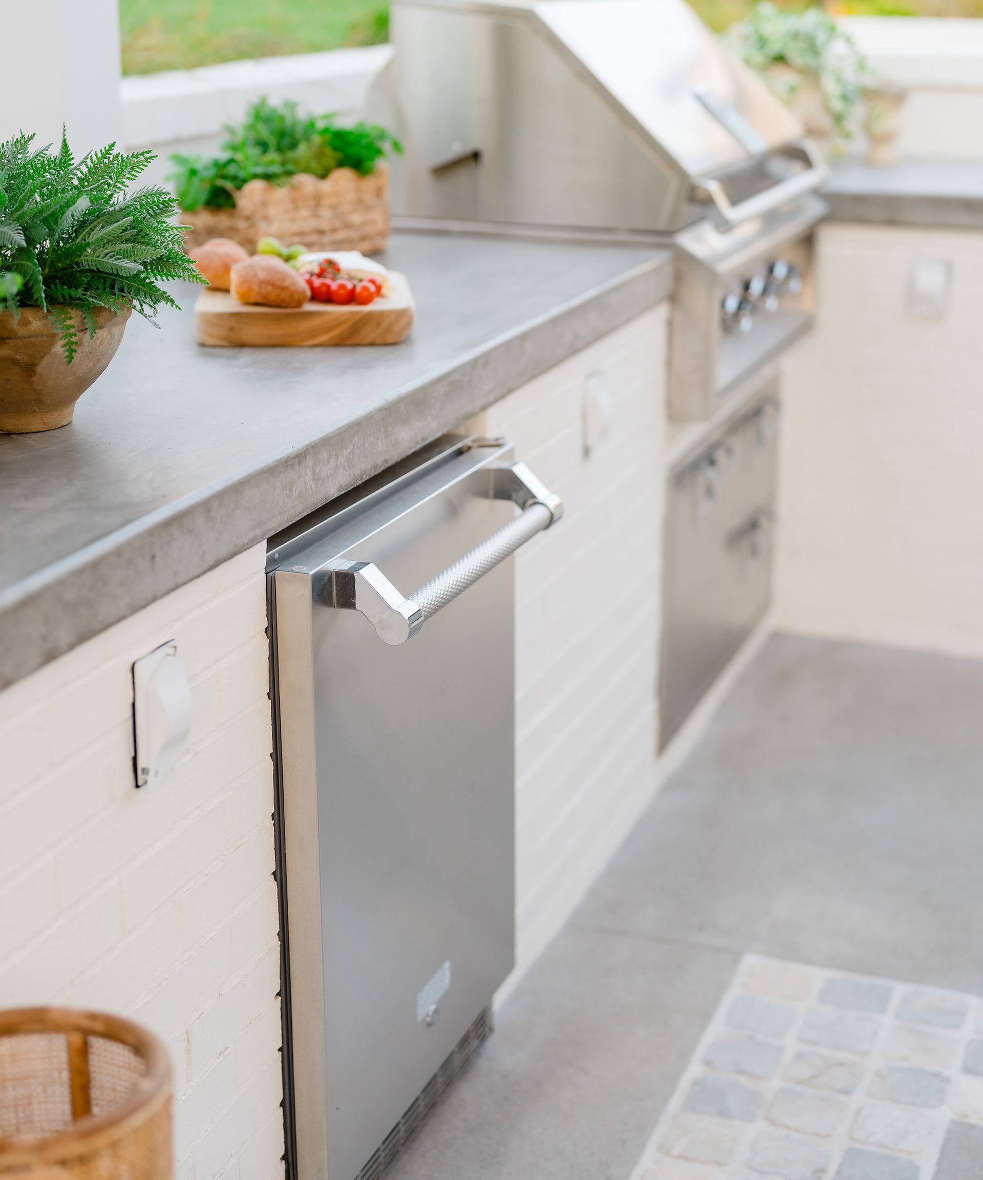 Close up of outdoor kitchen countertop with stainless steel appliances below and gray tile floor