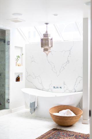 White bathroom with marble wall, white freestanding bath and jute towel basket