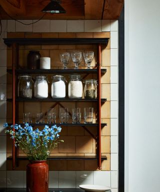 open shelf in kitchen with jars on and flowers on worktop
