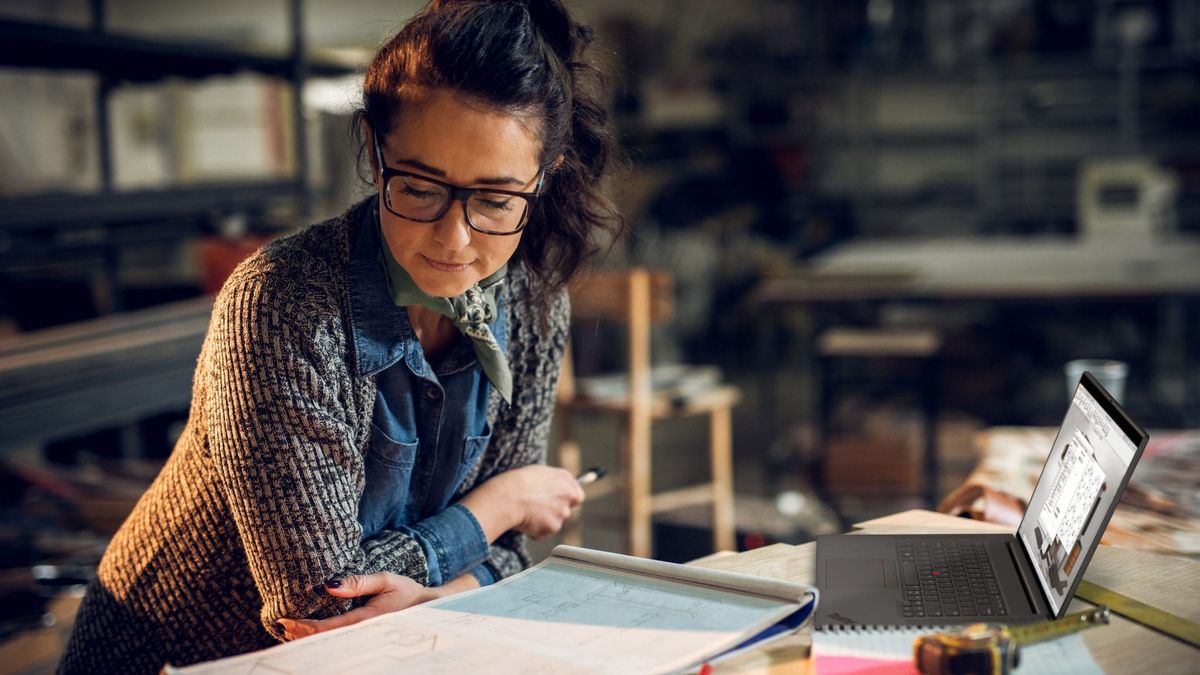 A bespectacled woman working at a cluttered desk with the Lenovo ThinkPad P1 Gen 4