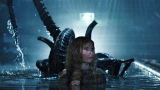 A young girl with long blonde hair is wading in water up to her armpits. She looks scared. Just behind her in the water is a dark, smooth-headed scary-looking alien with a sharp, whip-like tail. The alien (xenomorph) is getting ready to pounce on the girl.