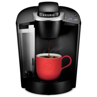 A black Keurig coffee maker with black coffee pouring into a red coffee cup