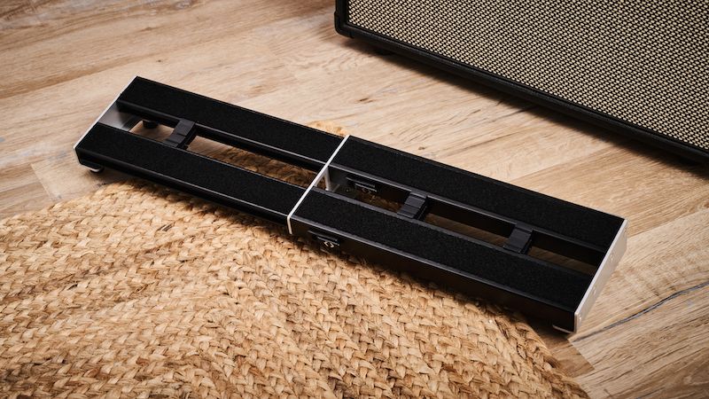 A D'Addario XPND1 pedalboard on a carpet in front of a guitar amp