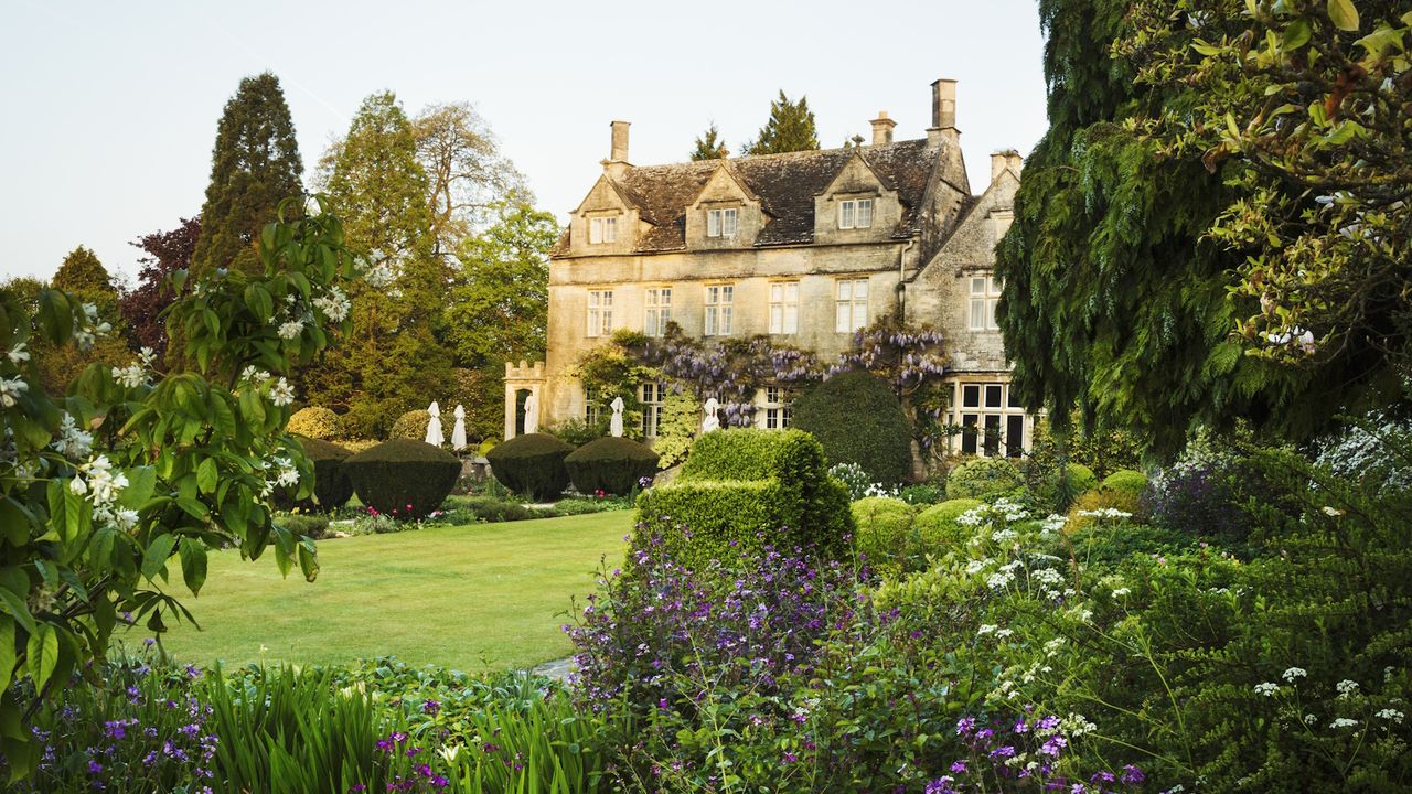 Exterior view of a 17th century country house from a garden with flower beds, shrubs and trees