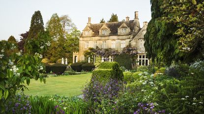 Exterior view of a 17th century country house from a garden with flower beds, shrubs and trees