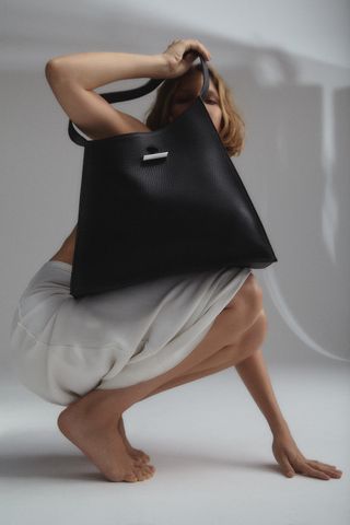 Woman in dress crouching with tote bag covering her face