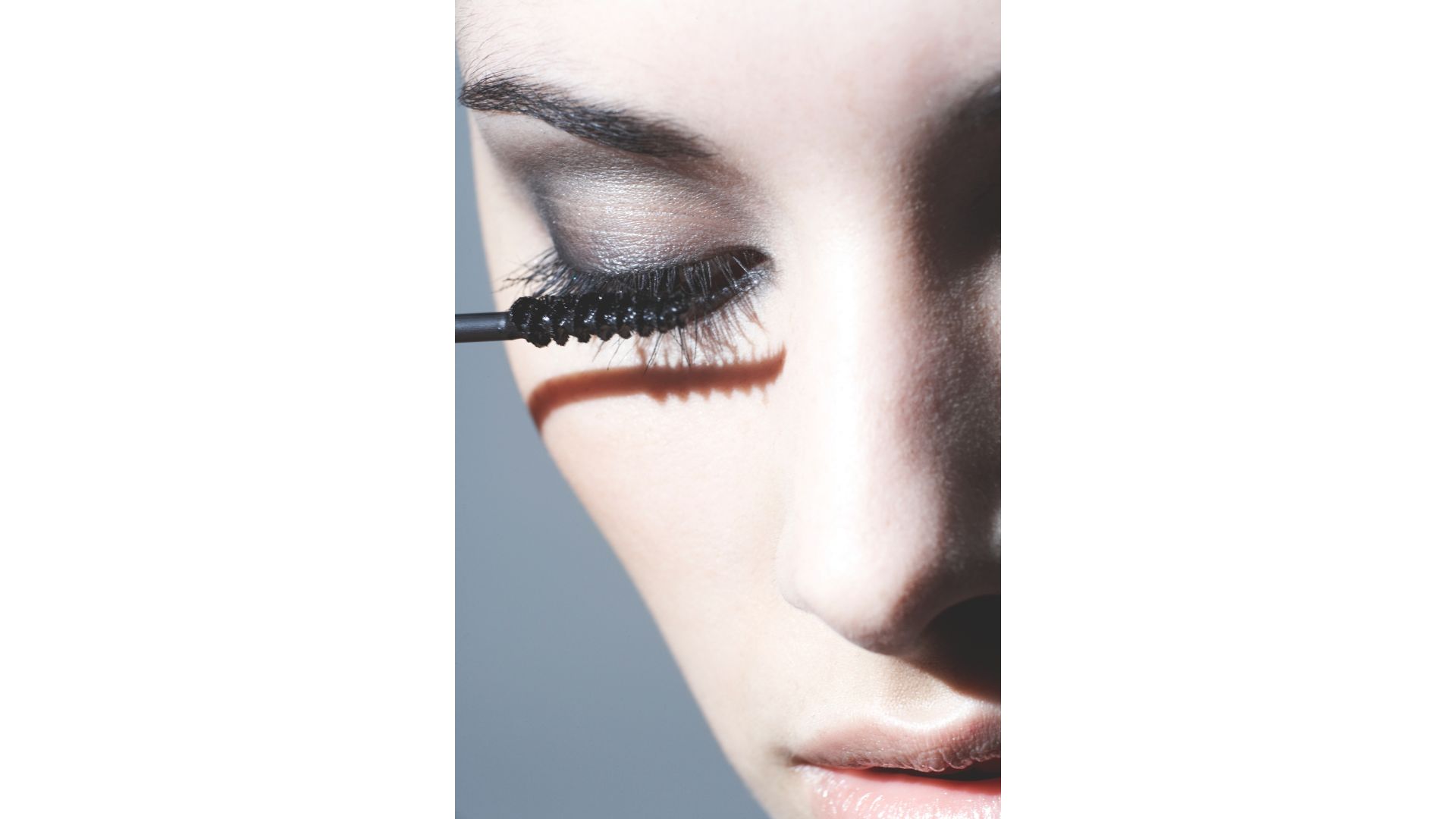 A woman's face, close up with a blue backdrop, applying eyeshadow on a smoky eye