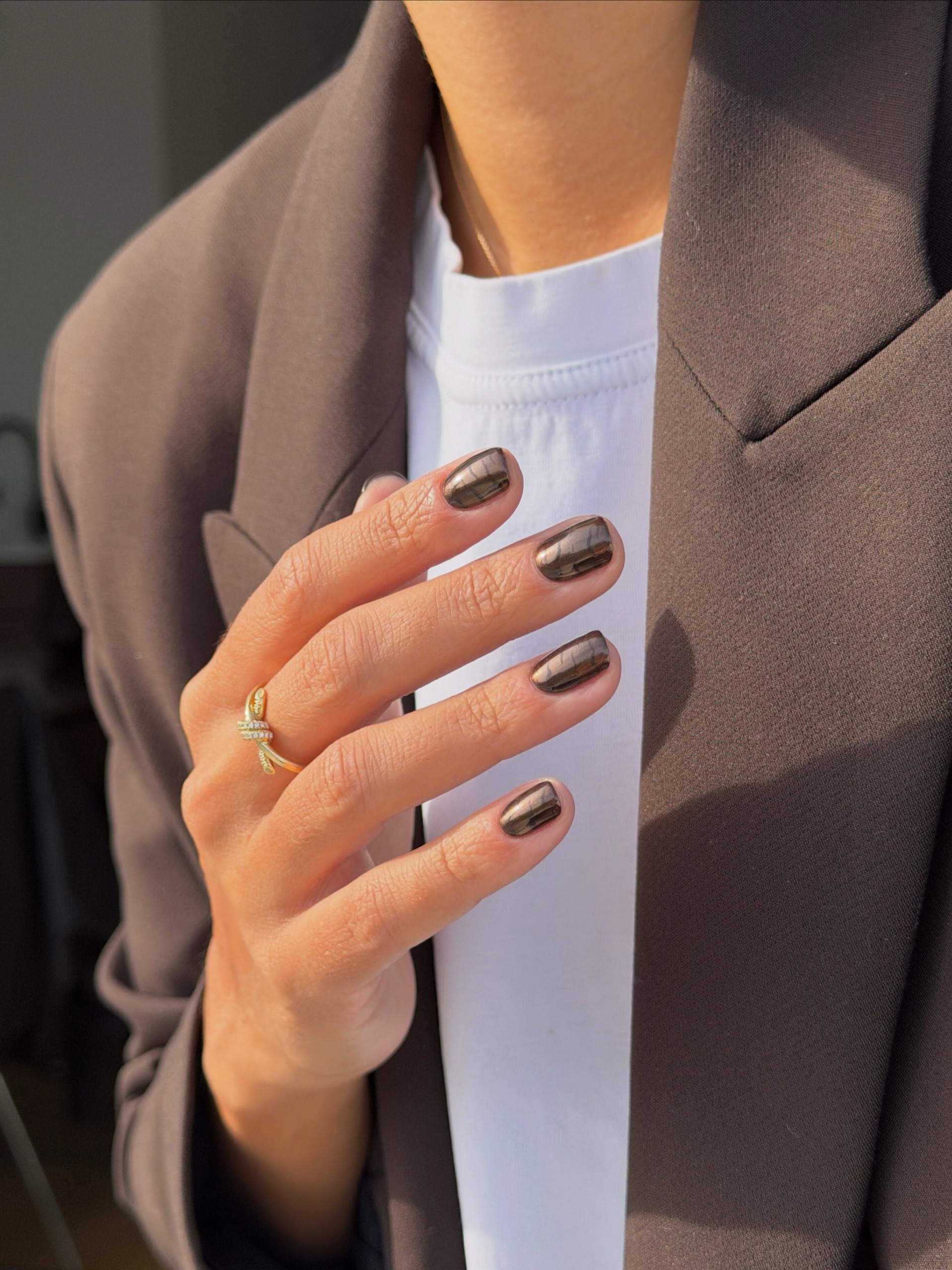 Short dark nails with subtle zebra stripes, hand against a brown blazer