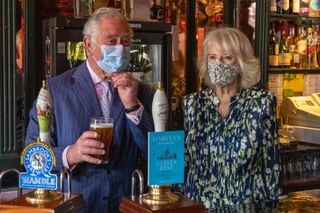 CLAPHAM, ENGLAND - MAY 27: Prince Charles, Prince of Wales pulls a pint of beer in a pub alongside Camilla, Duchess of Cornwall during a visit to Clapham Old Town on May 27, 2021 in Clapham, England. (Photo by Heathcliff O'Malley - WPA Pool/Getty Images)