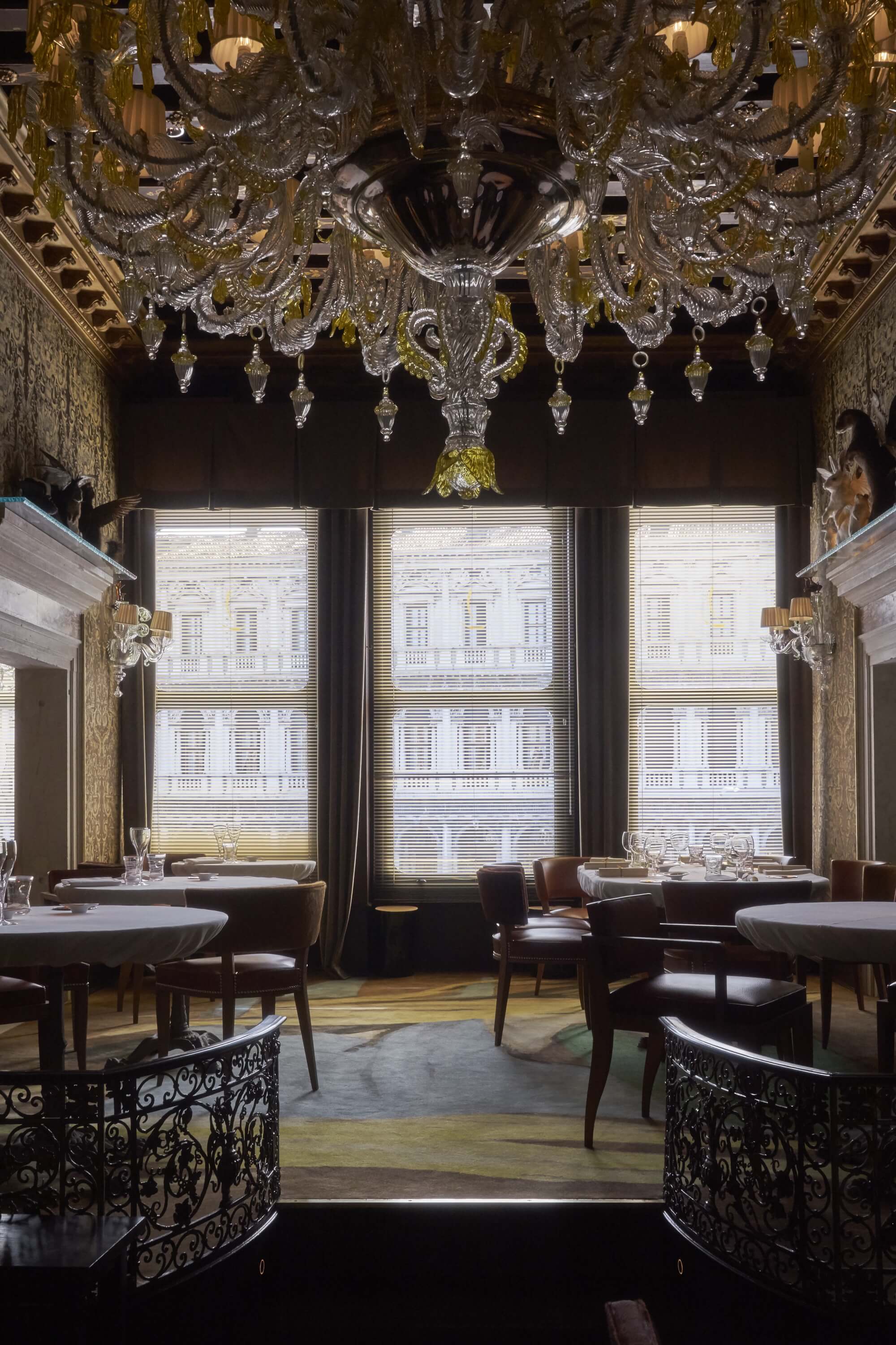 A transitional restaurant features palatial architectural features brought to life by contemporary interiors dotted in Murano glass, bordeaux leather, Art Nouveau wrought iron, and colorful carpets in ochre, light blue, and pale rose.