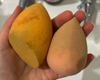 A hand holding two orange makeup sponges