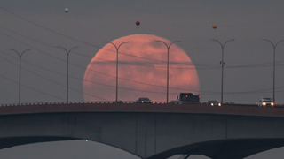 a red moon rising behind a bridge with traffic