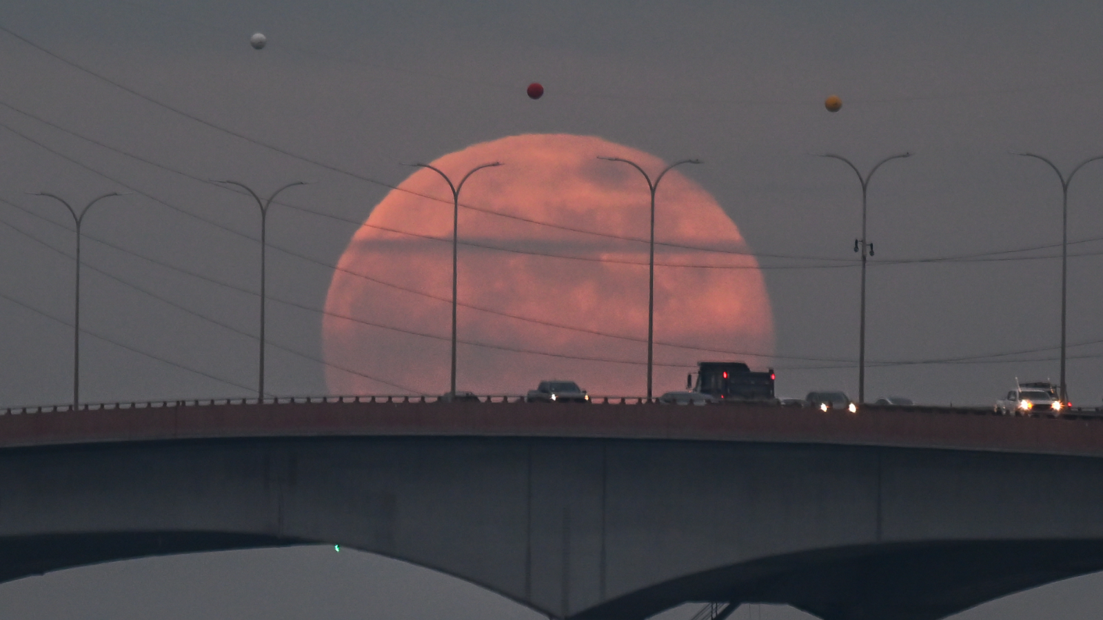 A red moon rises behind a bridge with traffic
