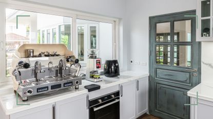a white modern kitchen with a green door, and kitchen appliances on the worktop including an air fryer and coffee machine, to illustrate where should you place an air fryer in your kitchen