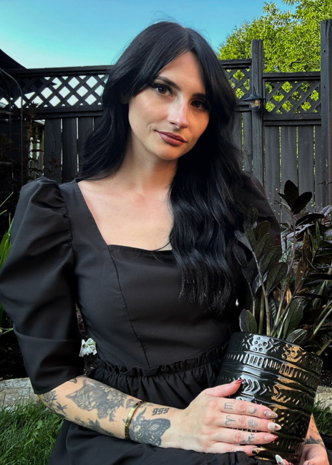A headshot of Chloe Hurst in a black dress holding a potted plant