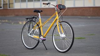A flat bar mixte bike leaning on a kickstand in an urban area, with the Swytch conversion kit fitted to the front of the bars