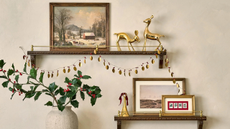 a holiday display with two shelves holding framed pictures, decorative objects, and a string of brass garland. A vase of holly branches sits on the left side of the image
