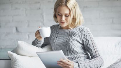 Woman looking at a tablet computer while holding a coffee cup.