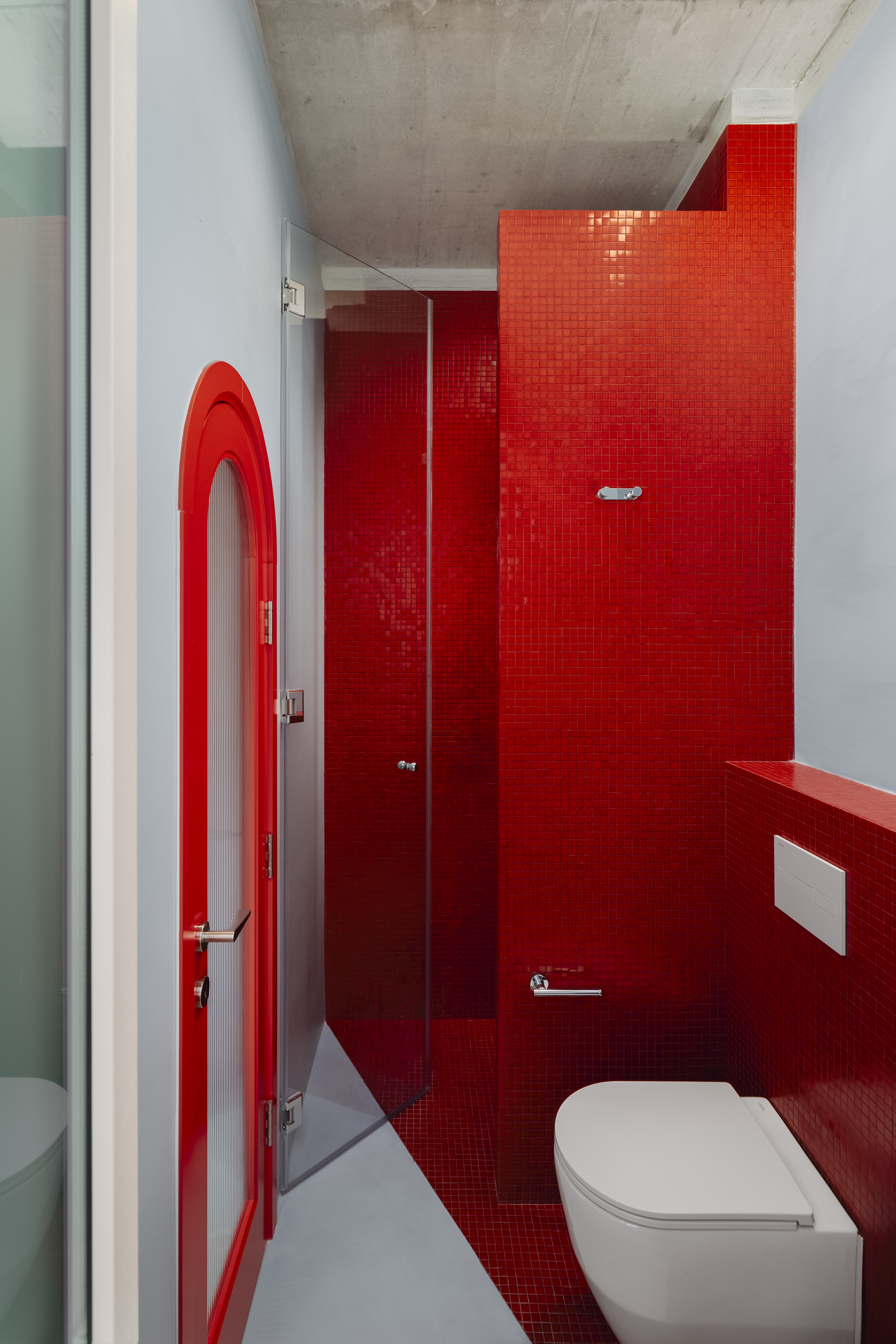 A bathroom with red mosaic walls, and red and gray flooring