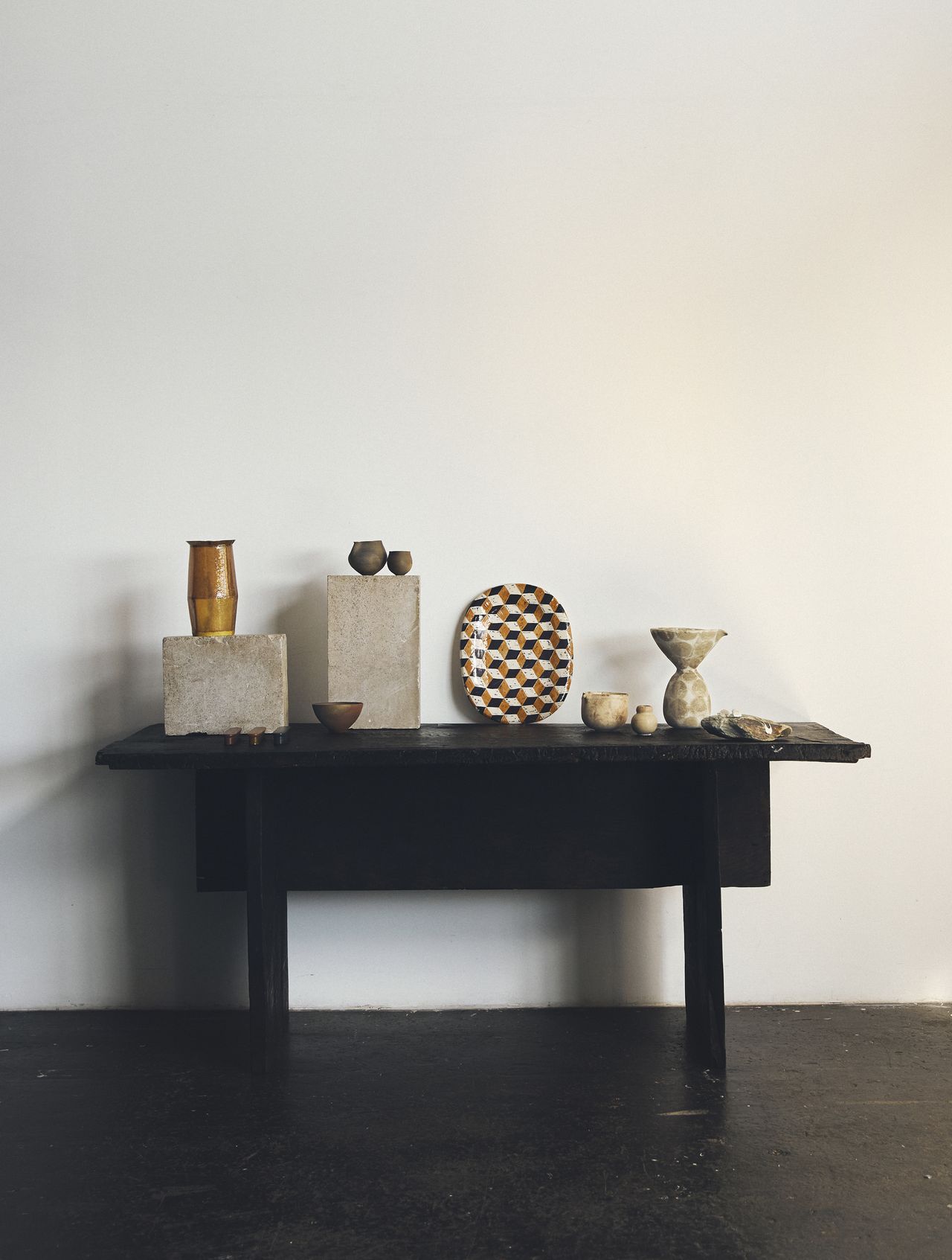 A black table in a white room that is styled with different artisan ceramics.