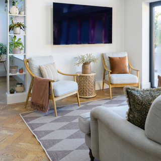 Grey sofa and grey geometir rug facing a TV on the wall. In fron of the TV is two chairs and a small table facing the sofa.