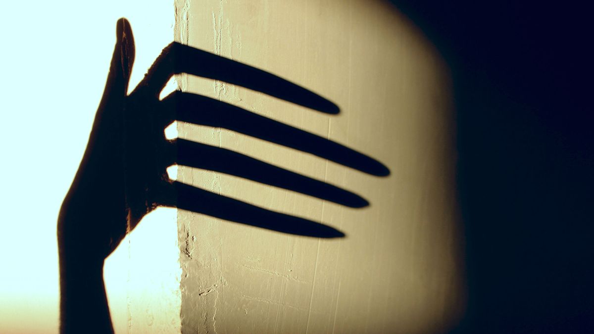 A spooky shadow of a hand reaches around a corner.