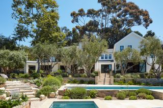 exterior of white rendered home with blue sky and planted garden with swimming pools