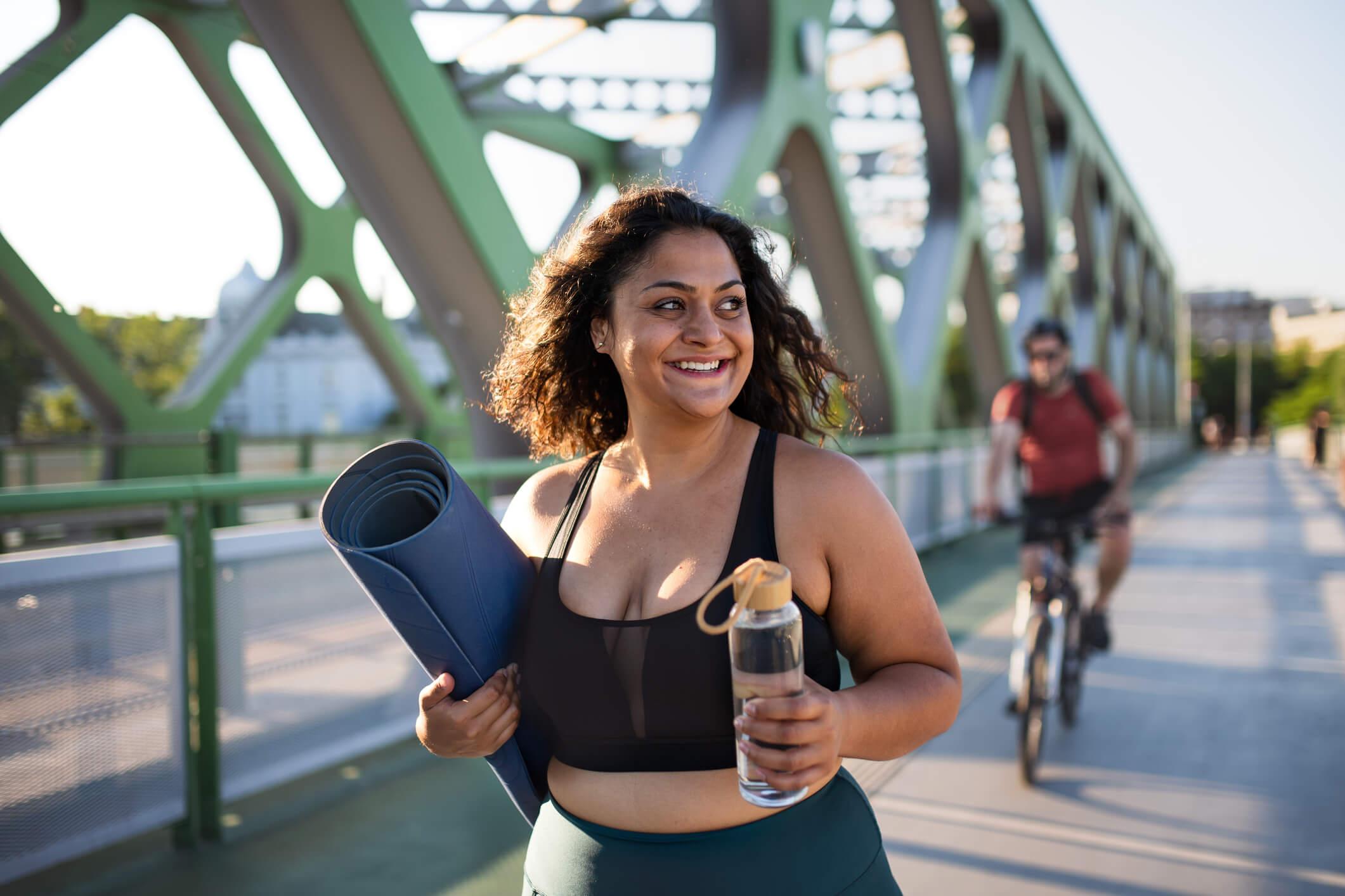  woman doing sport in city, carrying mat and water bottle 