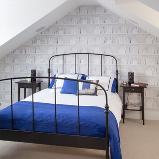 bedroom with white book shelf designed on wall cream colour floor and black metal bed with blue and white cushions