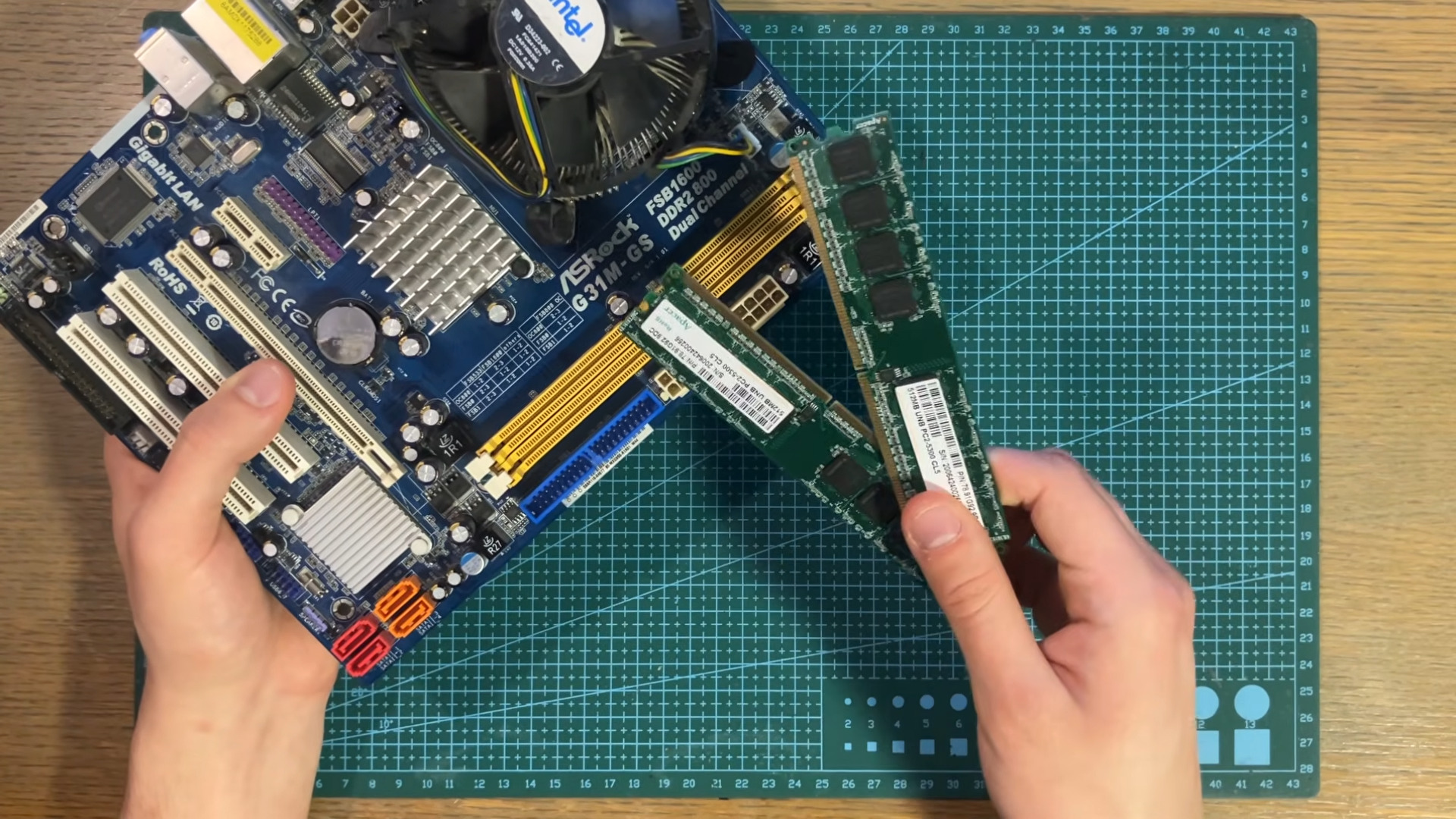 Some DDR2 RAM sticks being held up next to an old ASRock motherboard