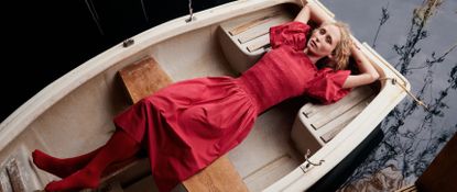 Hero banner of model wearing a red Liberty London dress lying in a wooden boat taken from above