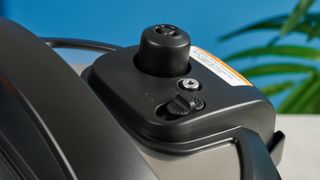 a black pressure cooker photographed against a blue background, showing its cooking presets, steam release valve, and Instant Pot branding