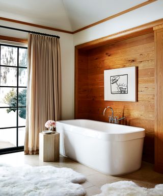Bathroom with freestanding bath, wooden cladding wall, flannel curtains and sheepskin rugs