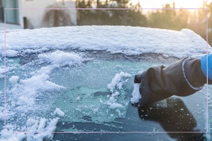 a close up of a hand de-icing a car windowscreen that is icy
